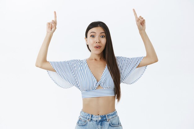 Porträt der aufgeregten und enthusiastischen charmanten asiatischen Freundin mit dunklem Haar in der kurzen Bluse, die Arme hebt