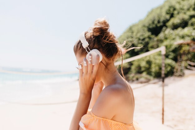 Porträt der bezaubernden Dame mit dunklem Haar, das an der Ozeanküste aufwirft. Erstaunliche gebräunte Frau, die im Sommer im exotischen Resort kühlt.