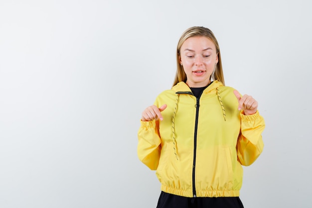 Porträt der blonden Dame, die im Trainingsanzug nach unten zeigt und erstaunte Vorderansicht schaut