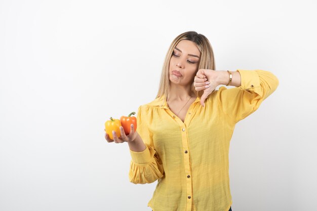 Porträt der blonden Frau, die bunte Paprika hält und Daumen nach unten gibt.