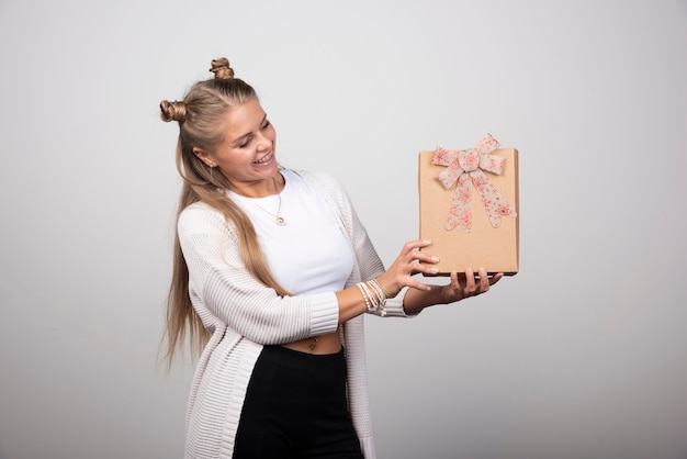 Porträt der blonden Frau Geschenkbox mit Bogen betrachtend.
