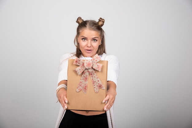 Porträt der blonden frau geschenkbox mit bogen zeigend.