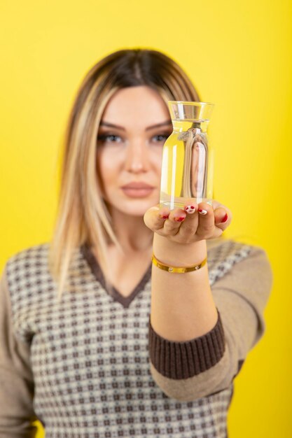 Porträt der blonden Frau mit einem Glas Wasser, das auf Gelb steht.