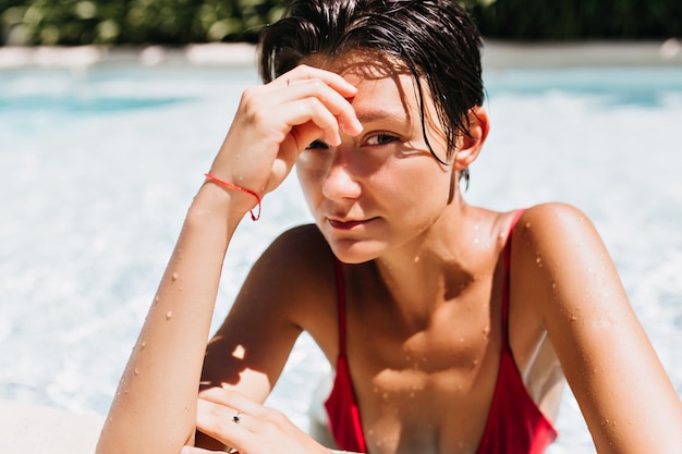 Porträt der braunhaarigen Frau mit gebräunter Haut, die im Pool sich entspannt.