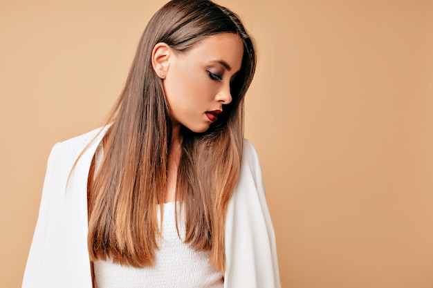 Porträt der eleganten entzückenden jungen schönen Frau, lokalisiert über beige Wand, schauendes Profil, konzentrierter Blick.