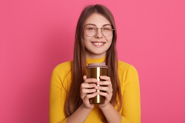 Porträt der entspannten jungen Frau, die drinnen steht und Tasse Kaffee hält, mit charmantem Lächeln