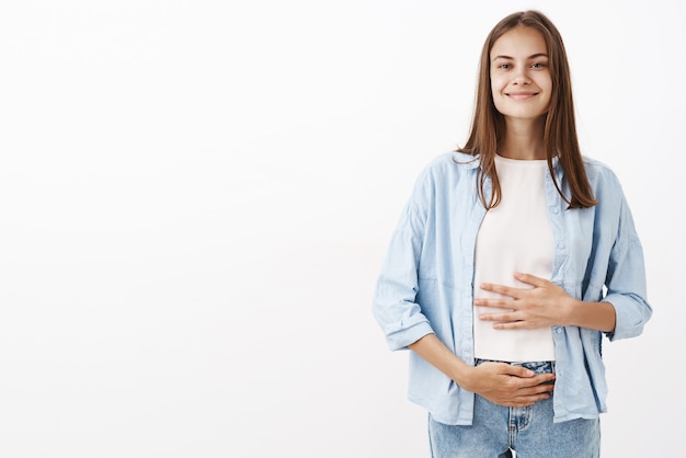 Porträt der entzückten freudigen jungen europäischen Frau, die sich um die Gesundheit kümmert, die Bauch oder Bauch mit erfreutem glücklichem Lächeln berührt, das Vitamine nimmt oder Joghurt trinkt