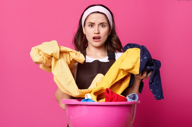 Porträt der erstaunten Frau mit dem riesigen rosa Becken mit frischer Kleidung und Heimtextilien