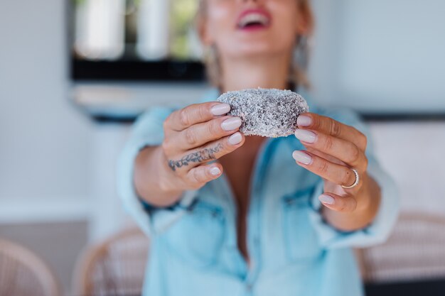 Porträt der europäischen Frau mit blondem Haar, das Donuts in der Küche zu Hause Villa genießt.