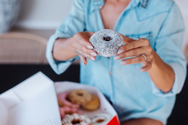 Porträt der europäischen Frau mit blondem Haar, das Donuts in der Küche zu Hause Villa genießt.