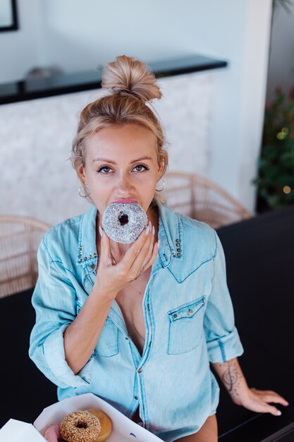 Porträt der europäischen Frau mit blondem Haar, das Donuts in der Küche zu Hause Villa genießt.