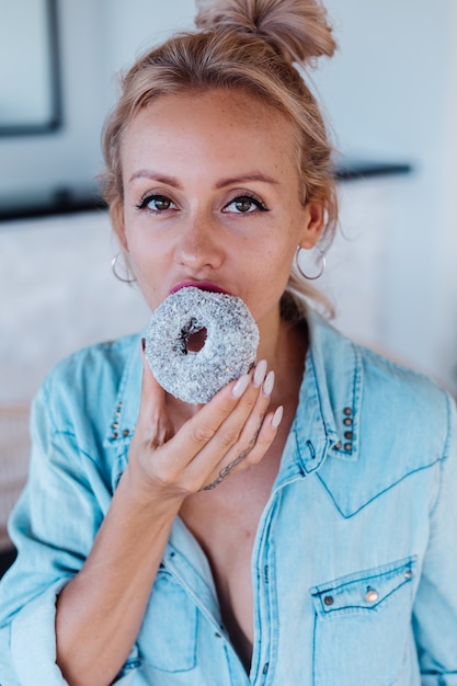 Porträt der europäischen Frau mit blondem Haar, das Donuts in der Küche zu Hause Villa genießt.