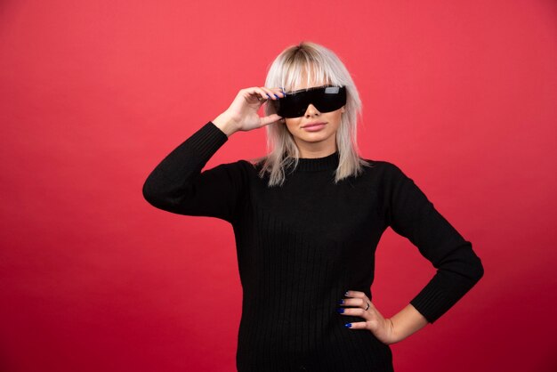 Porträt der Frau, die eine schwarze Brille auf einer roten Wand trägt.