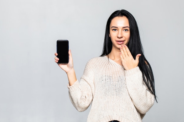 Porträt der Frau, die leeres sacreen Handy während des Stehens lokalisiert über grauer Wand zeigt