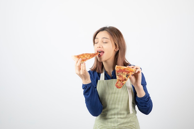 Porträt der Frau in der Küchenschürze, die Pizza auf Weiß isst