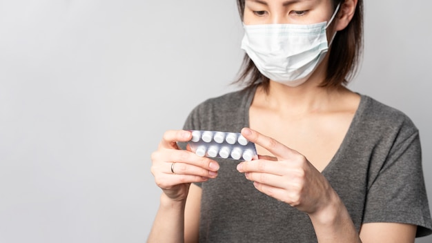 Porträt der Frau mit der chirurgischen Maske, die Tabletten prüft