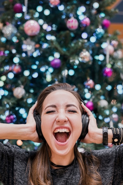 Porträt der frau mit kopfhörern und nahe weihnachtsbaum schreiend