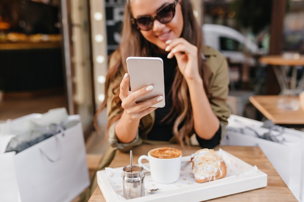 Porträt der gebräunten Dame mit eleganter Maniküre und Tasse Latte im Vordergrund