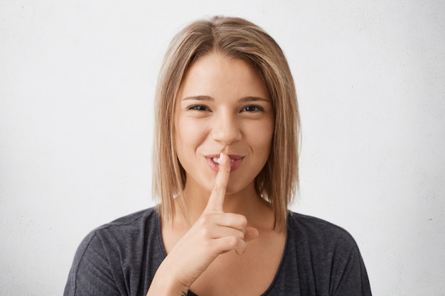 Porträt der geheimnisvollen positiven jungen Frau mit Finger auf den Lippen, die Stille Geste zeigen