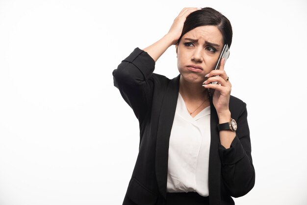 Porträt der Geschäftsfrau am Telefon sprechend auf weißer Wand.