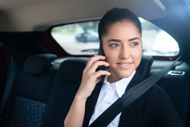 Porträt der Geschäftsfrau, die auf dem Weg zur Arbeit in einem Auto am Telefon spricht. Geschäftskonzept.