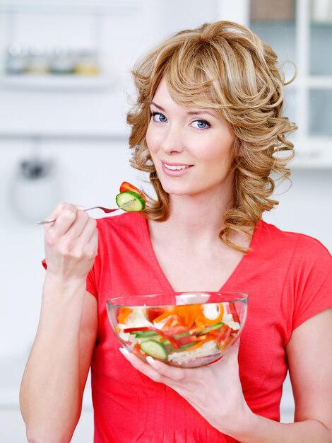 Porträt der glücklichen Frau, die den Salat des Gemüses in der Küche isst