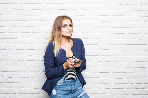 Porträt der glücklichen Frau, die gegen weiße Backsteinmauer lächelt und auf Handy plaudert.