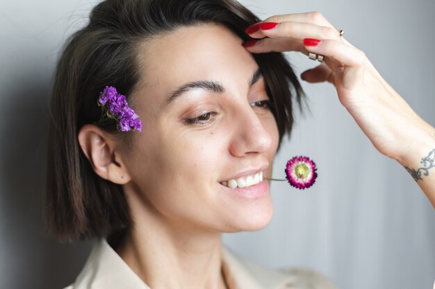 Porträt der glücklichen kaukasischen Frau ohne Make-up natürliche Schönheit, die getrocknete Blume grauweiß hält.