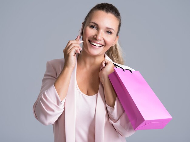 Porträt der glücklichen lächelnden Frau mit rosa Einkaufstasche, die auf einem Handy spricht.