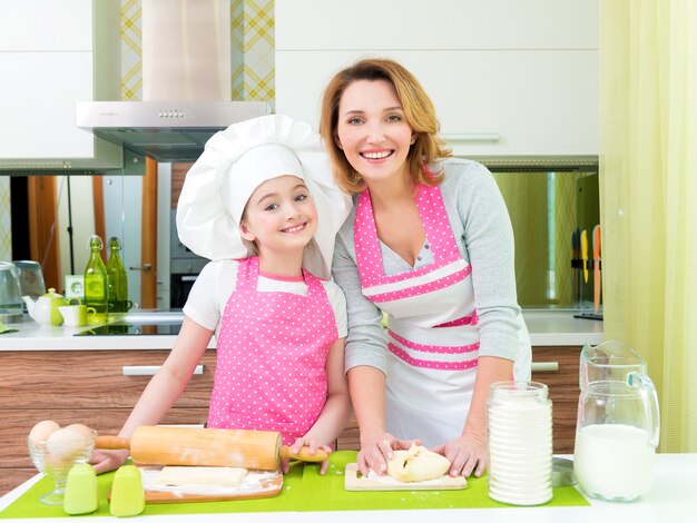 Porträt der glücklichen lächelnden Mutter und der Tochter, die zusammen Kuchen in der Küche machen.