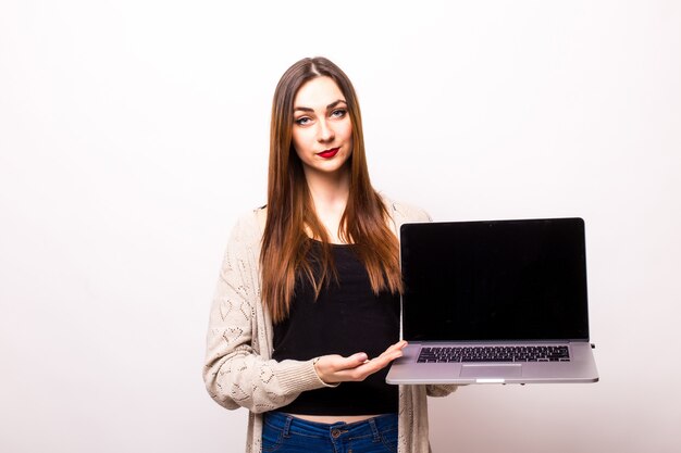 Porträt der glücklichen überraschten Frau, die mit Bildschirm des Laptops auf grau steht