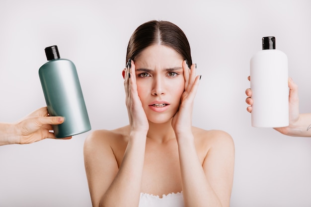 Porträt der grünäugigen Frau ohne Make-up auf isolierter Wand. Mädchen entscheidet, welches Shampoo besser zu verwenden ist.