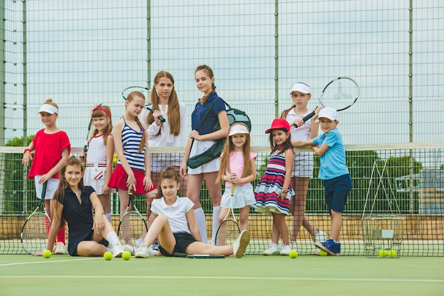 Porträt der gruppe von mädchen und jungen als tennisspieler, die tennisschläger gegen grünes gras des außenplatzes halten.