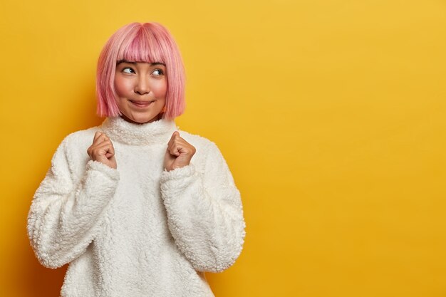 Porträt der gut aussehenden hoffnungsvollen Frau mit rosa Frisur erwartet für einige Ergebnisse geballte Fäuste trägt weißen warmen Pullover hofft auf positive Nachrichten Tagträume über den Sieg