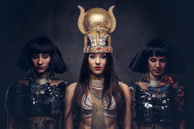 Kostenloses Foto porträt der hochmütigen ägyptischen königin in einem alten pharaokostüm mit zwei konkubinen. getrennt auf einem dunklen hintergrund.