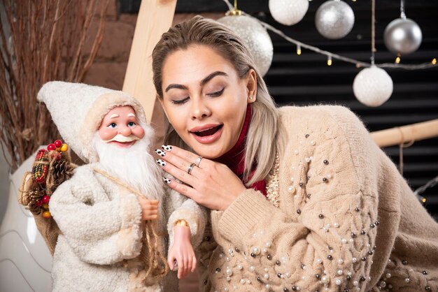 Porträt der hübschen Frau, die mit Weihnachtsmannspielzeug sitzt Hochwertiges Foto