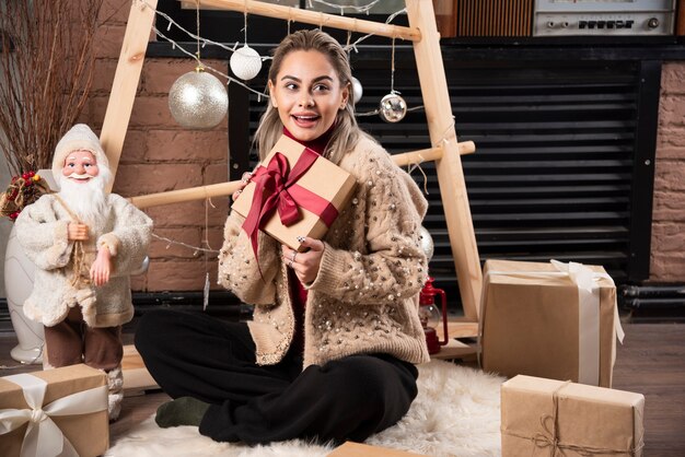 Porträt der hübschen Frau, die sitzt und ein Weihnachtsgeschenk hält