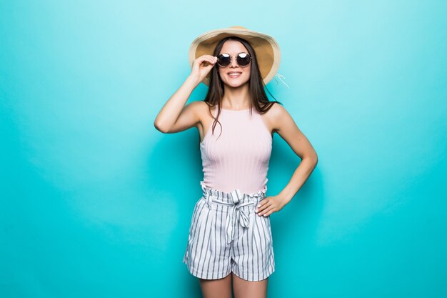 Porträt der hübschen Frau in der Sonnenbrille und im Hut über der blauen bunten Wand. Sommerberufung.