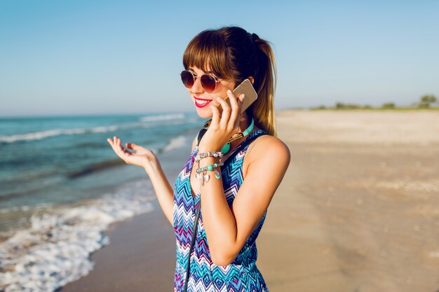 Porträt der hübschen Frau unter Verwendung des Smartphones am sonnigen Strand