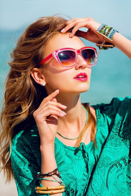 Porträt der hübschen jungen blonden schönen Frau in der kühlen Sonnenbrille, die auf dem sonnigen tropischen Strand aufwirft