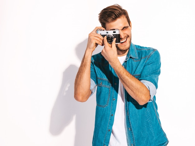 Porträt der hübschen lächelnden tragenden Sommerjeans des Mannes kleidet. Vorbildlicher Mann, der Foto auf alter Weinlesefotokamera macht.