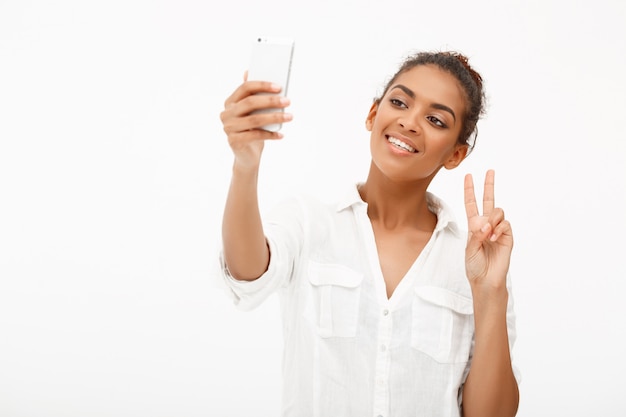 Porträt der jungen afrikanischen Frau, die selfie auf Weiß macht