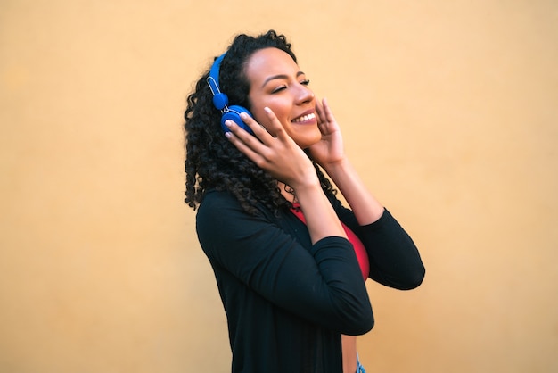 Porträt der jungen Afro-Frau, die Musik mit blauen Kopfhörern genießt und hört. Technologie- und Lifestyle-Konzept.