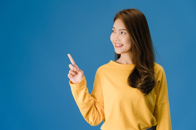 Porträt der jungen asiatischen Dame, die mit fröhlichem Ausdruck lächelt, zeigt etwas Erstaunliches an der leeren Stelle in der Freizeitkleidung und steht isoliert über blauem Hintergrund. Gesichtsausdruck Konzept.