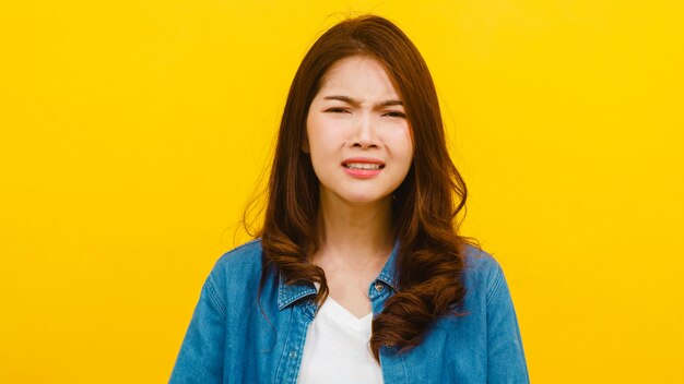 Porträt der jungen asiatischen Dame mit negativem Ausdruck, aufgeregtem Schreien, emotionalem Weinen wütend in lässiger Kleidung und Blick auf die Kamera über gelber Wand. Gesichtsausdruck Konzept.