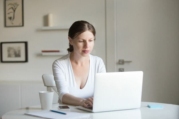 Porträt der jungen attraktiven Frau am Schreibtisch mit einem Laptop