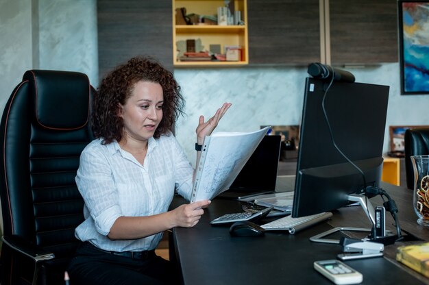 Porträt der jungen Büroangestelltenfrau, die am Schreibtisch mit Dokumenten sitzt, die sie nervös und gestresst betrachten, die im Büro arbeiten