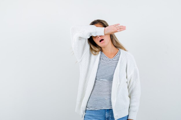 Porträt der jungen Dame, die Arm auf Augen im T-Shirt, in der Jacke und in der müden Vorderansicht hält