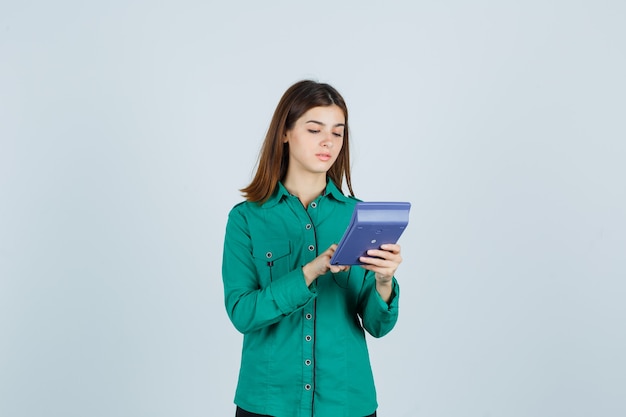 Porträt der jungen Dame, die Berechnungen auf Rechner im grünen Hemd macht und beschäftigte Vorderansicht schaut