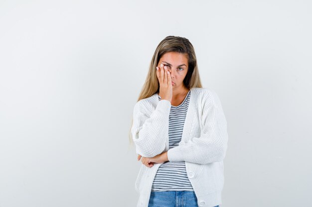 Porträt der jungen Dame, die Hand auf Wange im T-Shirt, in der Jacke und in der verärgerten Vorderansicht hält